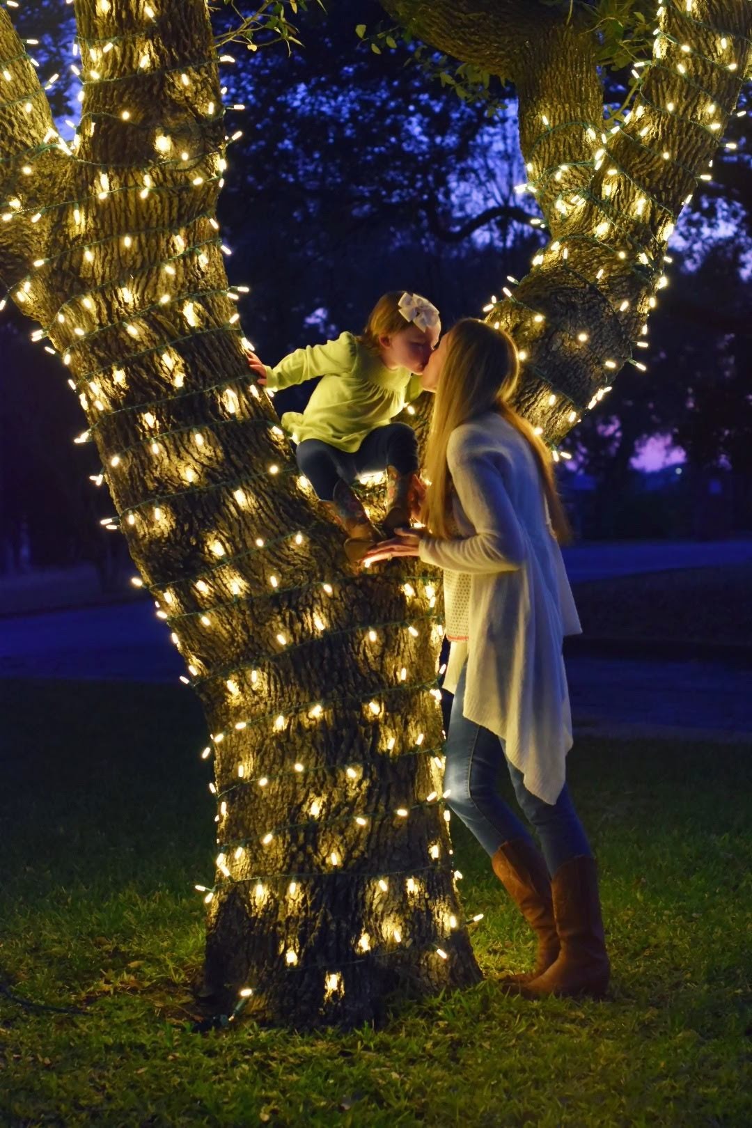 Mother and child beside a Texas tree wrapped in warm white Christmas lights